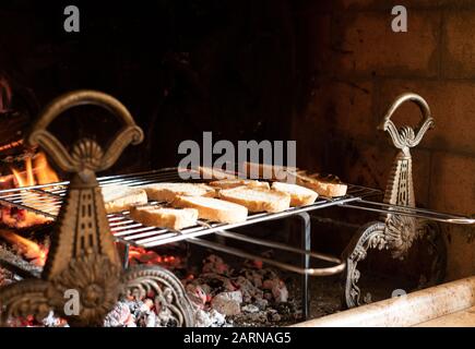 Assortiment de pain en tranches sur une grille métallique au-dessus de coals chauds et feu avec flammes dans une cheminée à l'intérieur avec espace de copie au-dessus Banque D'Images