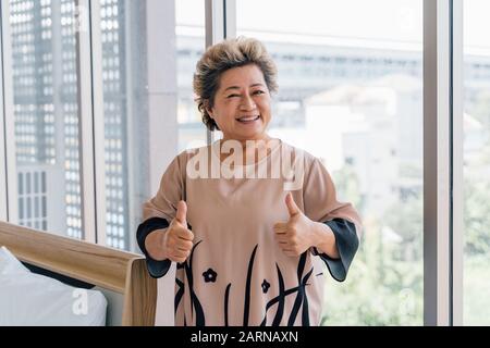 Une femme asiatique joyeuse souriante souriant et regardant la caméra tout en gardant les pouces élevés à l'hôpital moderne Banque D'Images