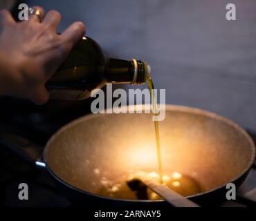 Verser de l'huile d'olive extra vierge dans une poêle chaude sur un cuiseur à gaz en vue rapprochée de la main du cuisinier et du liquide Banque D'Images