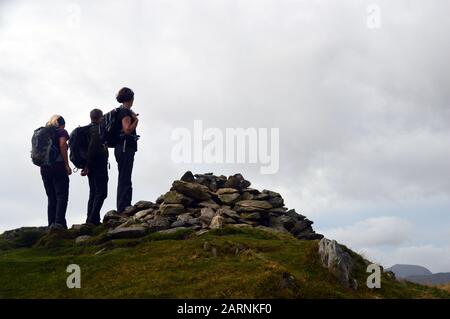 Trois Personnes se tenant par le sommet pile de Stones Cairn du Wainwright 'Arthurs Pike' dans le parc national du district du lac, Cumbria,. Angleterre, Royaume-Uni, Banque D'Images
