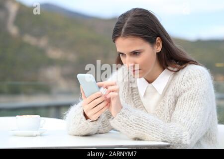 Une fille concentrée utilise un téléphone mobile assis sur une terrasse de café Banque D'Images