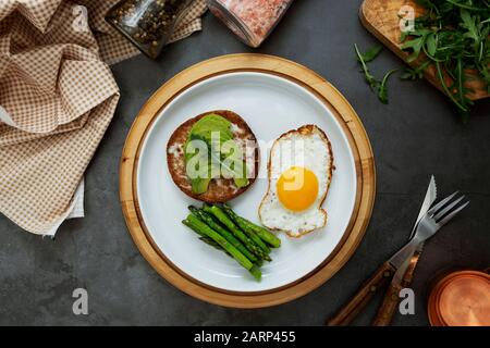 Sandwich grillé à l'avocat et un œuf frit sur une plaque blanche avec asperges. Nourriture ou petit déjeuner sains. Fond sombre. Banque D'Images