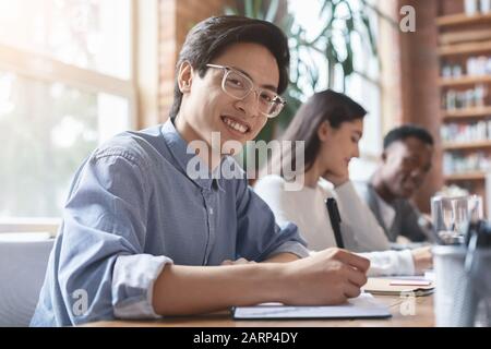 Un homme asiatique souriant prend des notes lors d'une réunion d'affaires avec ses collègues Banque D'Images