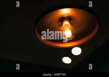 Lampe au tungstène vintage dans un abat-jour brillant en cuivre brillant dans une photo sombre et rapprochée avec mise au point sélective et DOF peu profond Banque D'Images