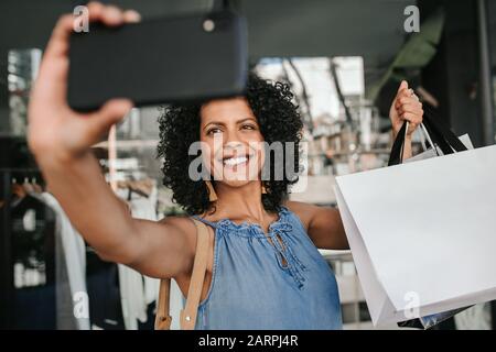 Une jeune femme souriante prend des selfies tout en faisant du shopping Banque D'Images