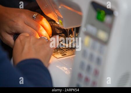 Couturière cousue des vêtements en tissu brun sur une machine à coudre, en travaillant à la lumière de la lampe matérielle intégrée, avec l'aiguille en acier avec une boucle et un pied de presse clairement visibles Banque D'Images