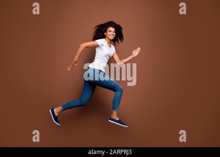 Photo pleine taille de la peau sombre étonnante dame sautant haut compétitions sportives rushing ligne finale gagnant humeur porter décontracté t-shirt blanc jeans Banque D'Images