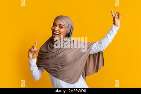 Joyeuse fille musulmane dans la danse et le chant hijab avec des mains levées Banque D'Images