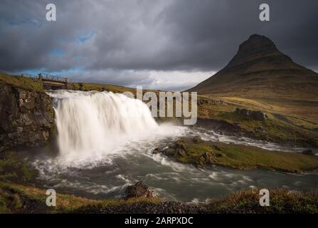 Un pont au-dessus de la cascade de Kirkjufellsfoss et près de la montagne épique Kirkjufell sur la côte nord de la péninsule d'Islande Snæfellsnes Banque D'Images