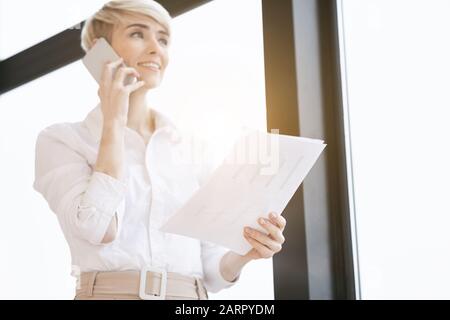 Lady Entrepreneur Parle Sur Téléphone Debout Près De La Fenêtre Au Bureau Banque D'Images