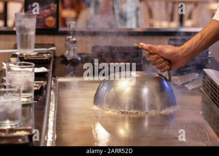 Cuisson sur une poêle japonaise, la surface de cuisson de Tepanyaki. La cuisinière a couvert les aliments de cuisson avec un couvercle et fait cuire les aliments à la vapeur. Gros plan Banque D'Images