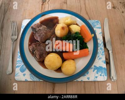 Déjeuner anglais dîner repas côtelettes d'agneau carottes bouillies et pommes de terre rôties épinards rouges sauce au vin blanc aux bords bleus sur une table en bois Banque D'Images