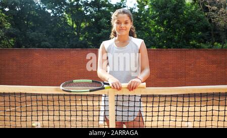 Portrait d'une jolie jeune fille de tennis debout avec raquette près du filet sur un court de tennis en argile orange Banque D'Images