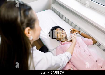 Examen échographique du cou dans la clinique. Femme médecin mène des recherches pour une jeune femme africaine souriante patient. Banque D'Images