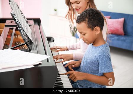 Femme enseignant à un petit garçon afro-américain de jouer du piano à la maison Banque D'Images