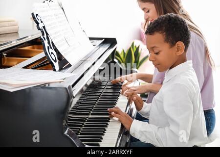 Femme enseignant à un petit garçon afro-américain de jouer du piano à la maison Banque D'Images