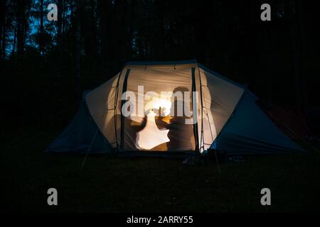 Silhouettes d'enfants jouant dans la tente de camping la nuit faisant des marionnettes d'ombre avec lampe de poche profiter des vacances d'été Banque D'Images