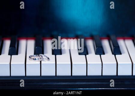 Une paire de bagues de mariage, son et ses, allongé sur un clavier de piano. Le piano est un accessoire pour une photographie de mariage à montrer au large des anneaux de platine Banque D'Images