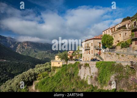 Nuages bas et lourds au-dessus des Gorges de Spelunca, maisons en pierre brigly éclairées à la colline d'Ota au-dessus du ravin , Corse-du-Sud, Corse, France Banque D'Images