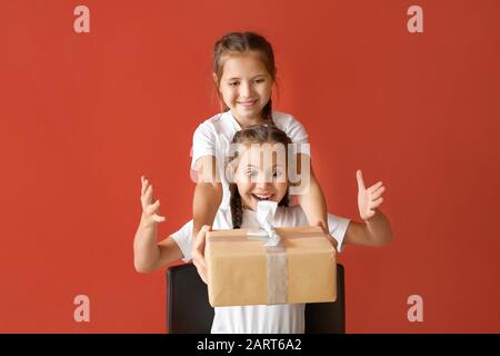 Jolie fille saluant sa sœur avec cadeau sur fond couleur Banque D'Images