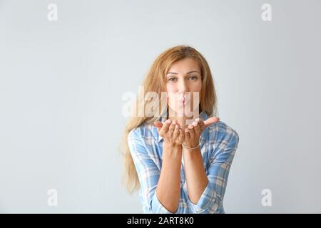 Belle jeune femme qui souffle baiser sur fond clair Banque D'Images