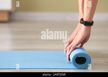 Jeune femme roulant tapis de yoga à la maison Banque D'Images