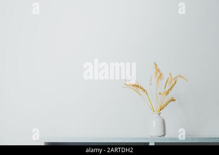 Spikelets ou blé dans un vase sur la table. Éléments de décoration maison dans un fond pastel clairsemé Banque D'Images
