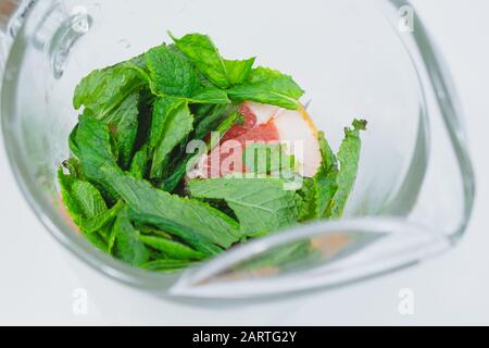 Feuilles de menthe poivrée fraîche et tranches de pamplemousse dans une vue rapprochée en verre. Préparation de l'eau tonique ou de la limonade, concept sain de boisson fraîche Banque D'Images