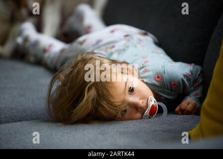 Jolie fille de bébé de 2 ans sur un lit sur son ventre avec la tête sur le canapé. Intérieur lumineux.