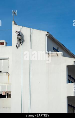 Rappel d'accès à la corde, réparation de bâtiments et peintre portant un harnais de sécurité complet sur le côté d'un bâtiment Banque D'Images