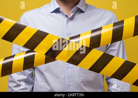 Homme se tenant derrière des lignes noires et jaunes de ruban adhésif qui interdit le passage. Concept d'absence d'entrée. Protection contre le coronavirus. Banque D'Images