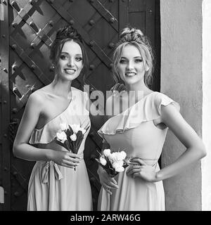 Deux belles filles mariées blondes et brunette femmes portant une élégante robe de demoiselle à l'épaule et tenant des bouquets de fleurs Banque D'Images