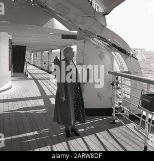 Années 1950, historique, une dame âgée passager dans son manteau debout à l'extérieur sur le pont d'un bateau à vapeur qui fait la tournée des fjords norvégiens en regardant l'océan environnant. Banque D'Images