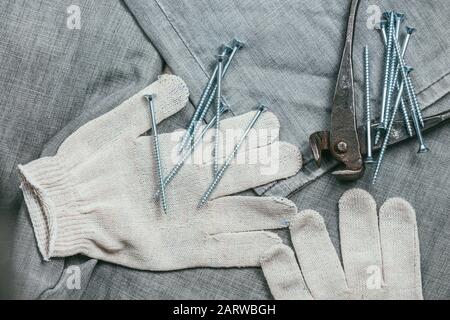 Une poignée de vis auto-coupantes métalliques et de pinces très anciennes et rouillées se trouvent sur les gants de travail tricotés de sécurité pour une utilisation industrielle sur fond de Banque D'Images