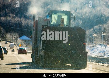 Une mise au point douce, avec chutes de neige légères et réfractions colorées, d'un camion articulé lourd transportant un tracteur agricole sur une route en hiver Banque D'Images