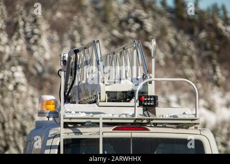 Gros plan à l'arrière d'une camionnette mobile avec échelle aérienne et lumière orange fixée au toit, neige recouverte en hiver avec fond flou Banque D'Images
