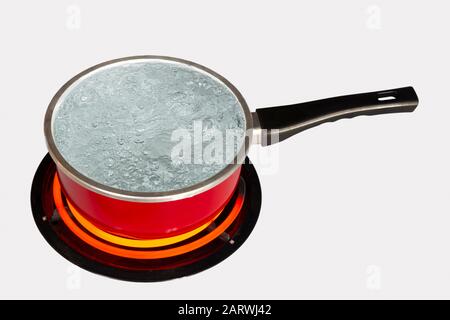 Tir horizontal regardant vers le bas sur un pot rouge d'eau bouillante sur le dessus d'une cuisinière avec le brûleur tourné vers le haut. Fond blanc. Espace de copie. Banque D'Images