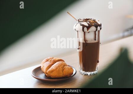 Verre de délicieux café à la frappe avec croissant sur table en bois Banque D'Images