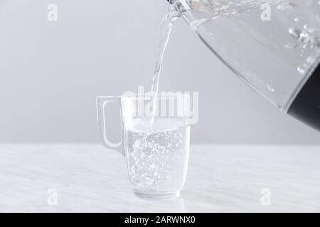 Verser de l'eau bouillie de la bouilloire électrique dans la tasse sur la table Banque D'Images