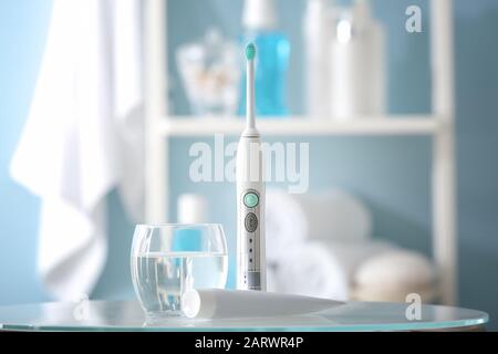 Brosse à dents électrique avec pâte et verre d'eau sur table dans la salle de bains Banque D'Images