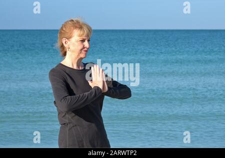 Femme mûre faisant du yoga au lever du soleil sur la plage Banque D'Images