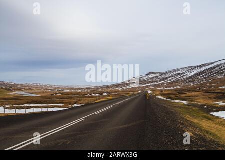 Route entourée de collines couvertes de neige et de verdure Sous un ciel nuageux en Islande Banque D'Images