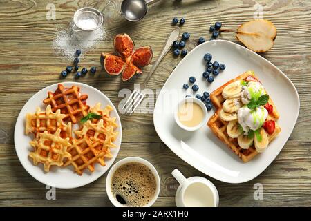 Assiettes avec gaufres savoureuses, crème glacée et café sur table en bois Banque D'Images