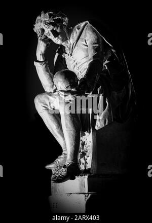 Statue dans les jardins de Bancroft, Stratford-upon-Avon, du personnage shashararéen Hamlet tenant le crâne de Yorick, illuminée la nuit. Noir et blanc. Banque D'Images