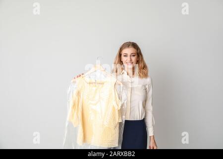 Femme de nettoyage à sec moderne avec des vêtements sur fond clair Banque D'Images