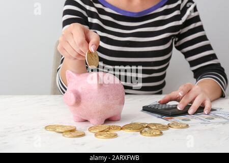 Femme mettant une pièce de monnaie dans la banque piquante et comptant de l'argent à table Banque D'Images