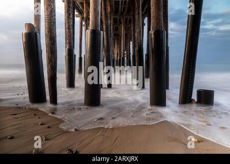 Gros plan des piliers, Ventura Pier, Ventura, Californie. Lumière tôt du lever du soleil visible de gauche. Sable et rochers en premier plan. Banque D'Images