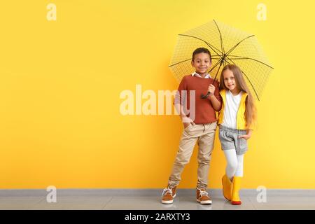 Tendance petits enfants en vêtements d'automne et avec parapluie près du mur de couleur Banque D'Images