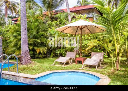 Piscine avec parasol et lits de plage dans un hôtel tropical ou une maison résidentielle. Belle piscine dans la cour en été. Piscine avec eau bleue propre dans a b Banque D'Images