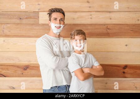 Père et son petit fils avec de la mousse à raser sur leurs visages sur fond de bois Banque D'Images